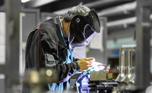 Industrial worker with protective mask welding inox elements in steel structures manufacture workshop or metal factory.